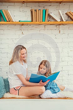 Happy caucasian mom with her daughter reading a book and smiling