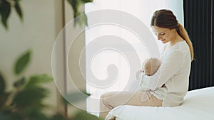 Happy caucasian mother breastfeeding newborn baby sitting on the bed. Concept breast feeding and lactation infant