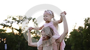 Happy caucasian mother carries beautiful little daughter on her shoulders, dancing and having fun together in public