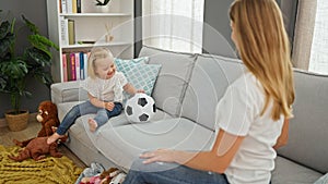 Happy caucasian mother and daughter playing ball together, sitting comfortably on living room sofa, indoors at home