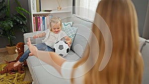 Happy caucasian mother and daughter playing ball together, sitting comfortably on living room sofa, indoors at home