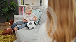 Happy caucasian mother and daughter playing ball together, sitting comfortably on living room sofa, indoors at home. smiling,