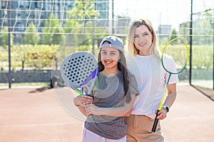 Happy caucasian mother and daughter playing padel tennis and badminton on tennis court outdoors