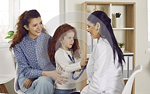 Happy Caucasian mother with daughter at reception of woman doctor, baby girl plays with stethoscope