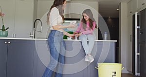 Happy caucasian mother and daughter segregating rubbish in kitchen