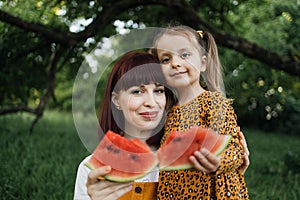 Happy caucasian mother and her cheerful daughter eating watermelon in summer day outdoor