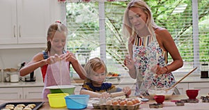 Happy caucasian mother in kitchen with daughter and son, wearing aprons baking cookies together