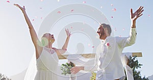 Happy caucasian newly wed couple, jumping throwing petals in front of altar outdoors