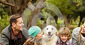 Happy caucasian parents, son and daughter lying with pet dog in park