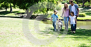 Happy caucasian parents, son and daughter walking with pet dog in park