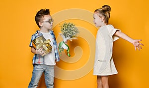 Happy caucasian people boy gives a flowers to his girlfriend isolated over yellow background.