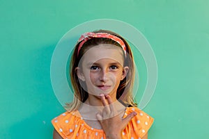 Happy caucasian schoolgirl doing sign language gesture over blue background at elementary school