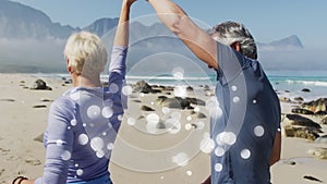 Happy caucasian senior couple dancing on beach, over moving bokeh light spots