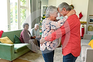 Happy caucasian senior couple dancing in front of their diverse friends at christmas time