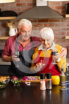 Happy caucasian senior couple preparing vegetables, drinking wine, embracing in kitchen, copy space
