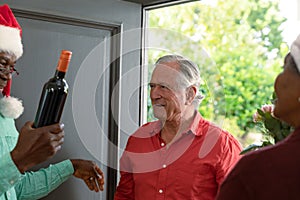 Happy caucasian senior man with wine coming to visit diverse friends at christmas time