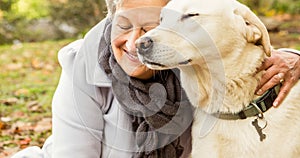 Happy caucasian senior woman embracing golden retriever pet dog in park