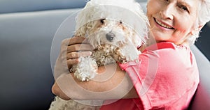 Happy caucasian senior woman holding small white pet dog and smiling