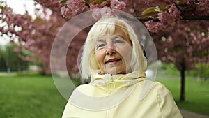 Happy Caucasian senior woman looking at camera in the park for outdoor walk or mindset for wellness city park. Beautiful