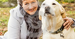 Happy caucasian senior woman smiling and embracing pet labrador dog in park