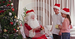 Happy caucasian siblings with santa claus giving presents at christmas