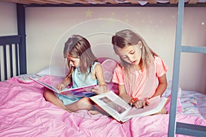 Happy Caucasian sisters girls reading books in the bedroom. Children siblings at home spending time together. Kids education