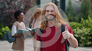 Happy Caucasian student guy man male schoolboy in city outdoors university college campus showing thumbs up to camera