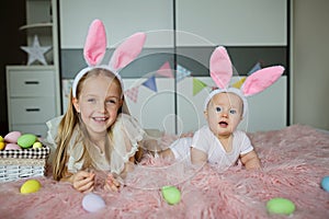 happy caucasian toddler girl 7 years old and her baby sister 6 months old wearing bunny ears headband, lying on bed at
