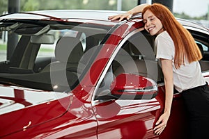Happy caucasian woman embracing her new car at auto dealership