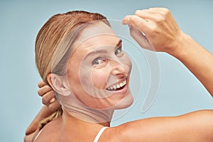 Happy caucasian woman looking back and posing at camera while standing over beige background