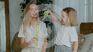 Happy Caucasian woman mum and cute little kid daughter child girl blowing soap bubbles at home mother helping adorable