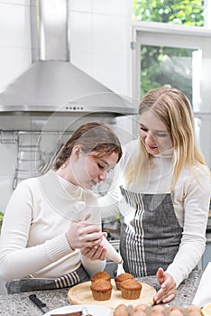 Happy Caucasian Young Mother and Teenage Daughter dressing delicious homemade cream on cupcake in kitchen