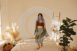 Happy caucasian young woman jumping on mattress in modern living room interior.
