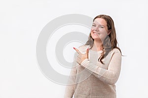 Happy caucasian young woman in sweater smiling broadly at camera, pointing fingers away, showing something interesting