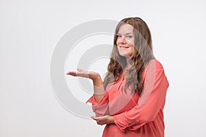 Happy caucasian young woman in sweater smiling broadly at camera, pointing fingers away, showing something interesting