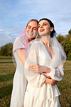 Happy charming bride in a white dress with a white veil and a bridesmaid in a light blue dress with pink veil gently