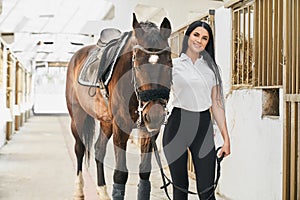 Happy charming woman standing near strong purebred horse