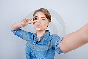 Happy charming young girl taking self portrait showing v-sign an