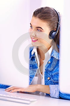 Happy charming young woman sitting and working with laptop using headset in office