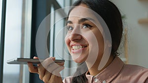 Happy cheerful Arabian Indian business girl talk mobile phone near window female businesswoman woman say on speakerphone