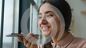 Happy cheerful Arabian Indian business girl talk mobile phone near window female businesswoman woman say on speakerphone