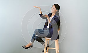 Happy cheerful Asian business woman in navy blue suit presenting or showing open hand palm with copy space for product while