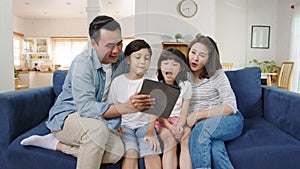 Happy cheerful Asian family dad, mom and kids having fun and using digital tablet video call on sofa at house. Self-isolation,