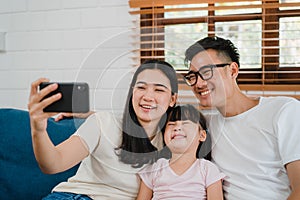 Happy cheerful Asian family dad, mom and kids having fun and using smart phone video call on sofa at house. Self-isolation, stay