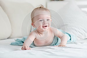 Happy cheerful baby boy covered in blue towel after washing in bath