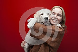 Happy cheerful beautiful girl holding a dog on a red background, a woman hugs a golden retriever puppy and smiles, people with