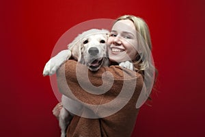 Happy cheerful beautiful girl holding a dog on a red background, a woman hugs a golden retriever puppy and smiles, people with