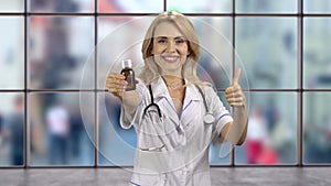 Happy cheerful blonde woman gives you a medicine bottle and her thumb up.