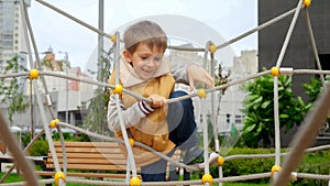 Happy cheerful boy climbing through ropes and nets on the public playground. Active child, sports and development, kids playing