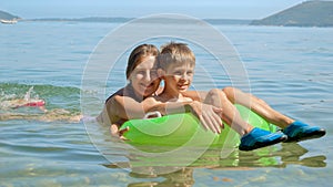 Happy cheerful boy and mother swimming with inflatable ring in calm sea waves towards the beach